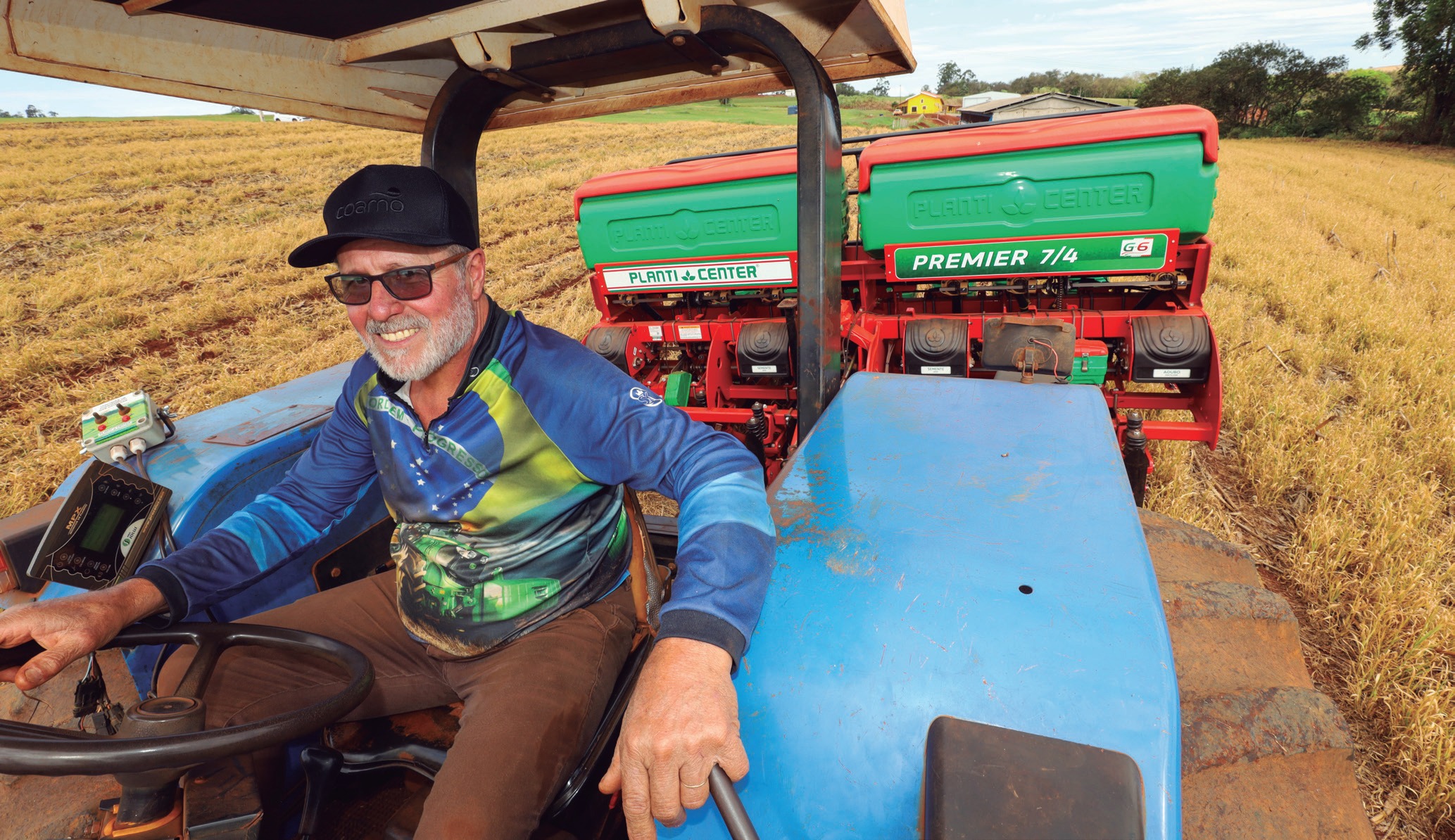 Cooperado sorrindo ao volante de um trator azul com plantadeira vermelha e verde