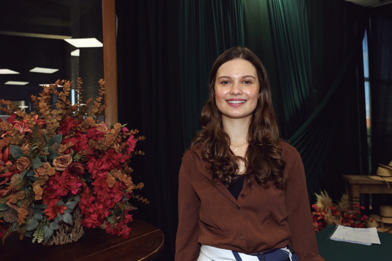 Ana Carolina Frabi Am&eacute;rico, de blusa marrom, diante de arranjo de flores