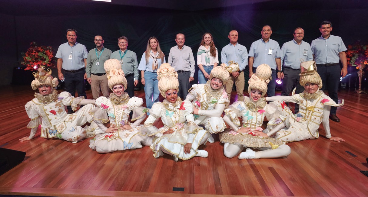 Gerentes e diretores da Coamo e da Credicoamo em p&eacute; atr&aacute;s de um grupo de dan&ccedil;arinas sentadas no palco