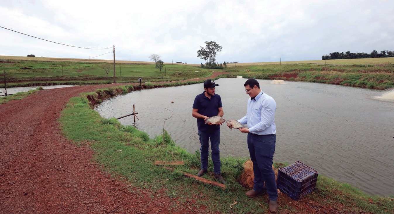 Engenheiro de pesca ao lado de tanque de piscicultura, ao lado de outro homem
