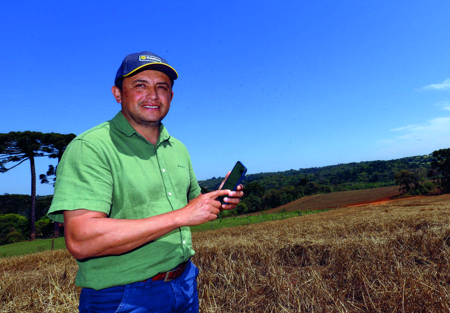 Homem em um campo, sorrindo e segurando um smartphone.