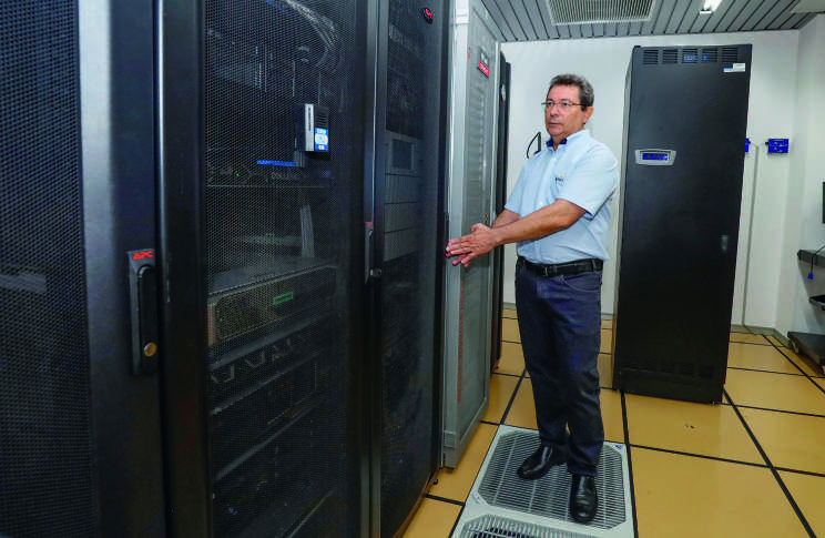 Homem em uma sala de servidores, ao lado de grandes racks de computadores.